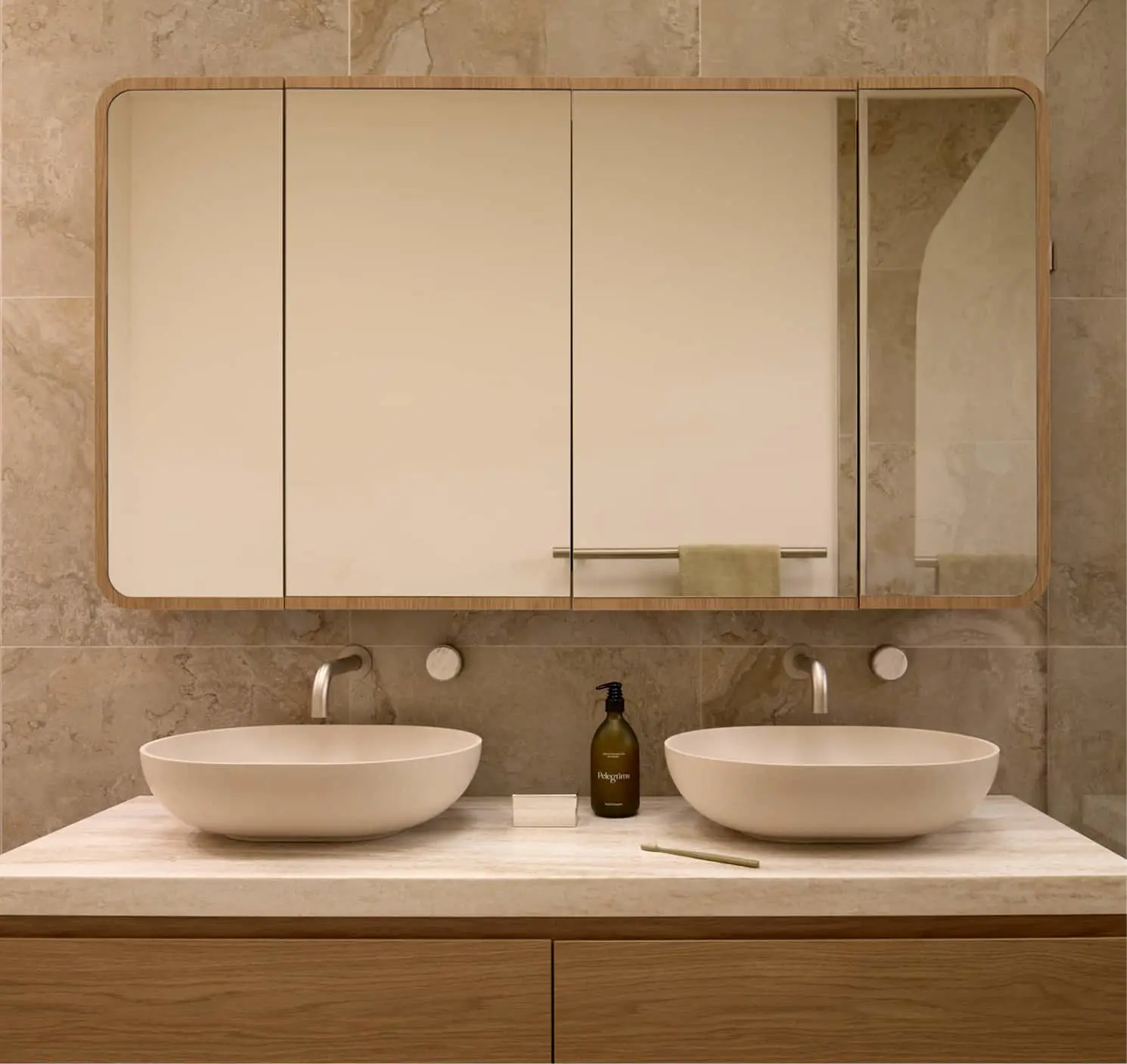Modern bathroom vanity with two white oval sinks, wall-mounted faucets, and a large mirror cabinet against beige tile.