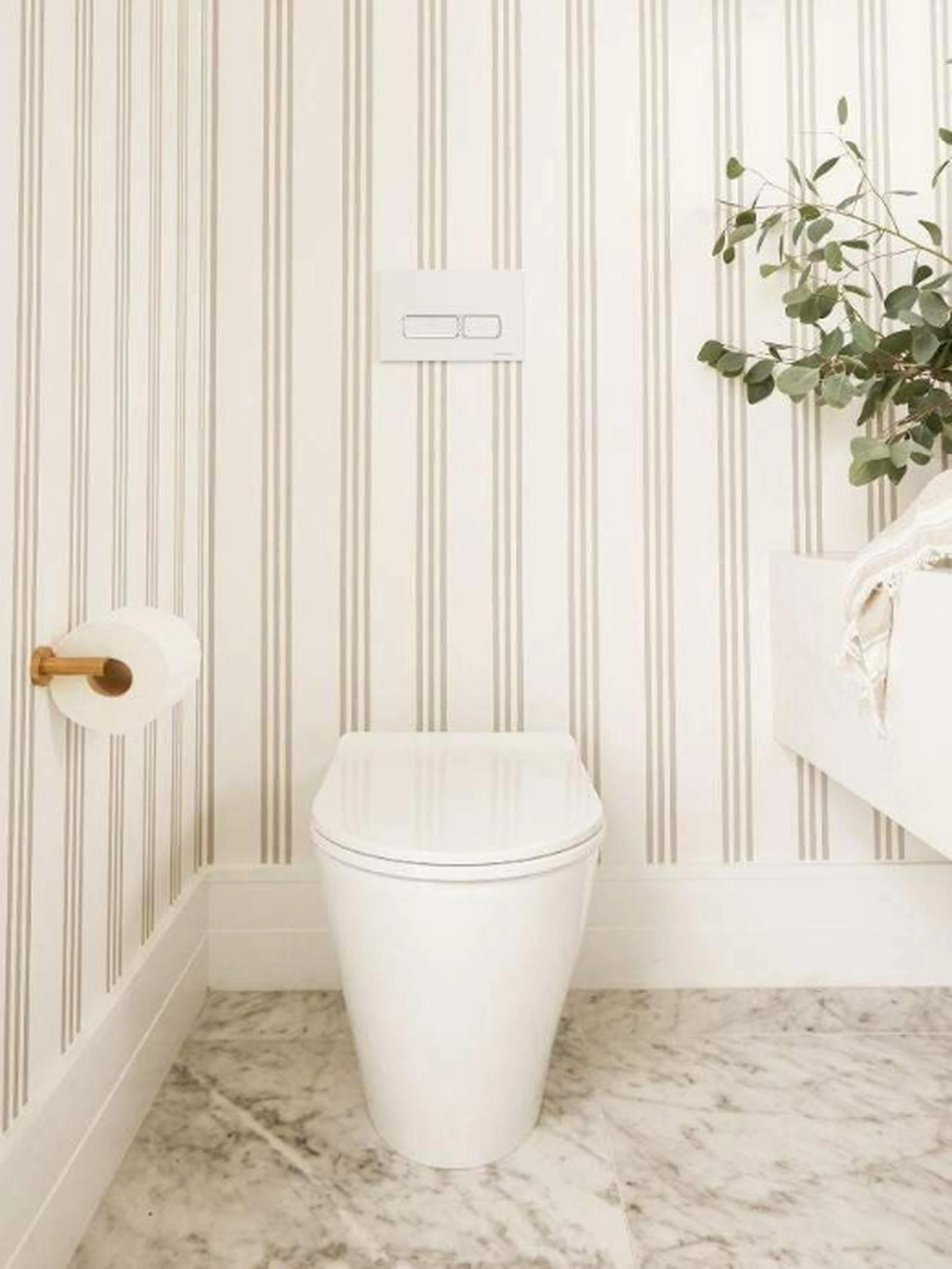 Modern bathroom with white toilet, striped wallpaper, marble floor, and green plant in corner.