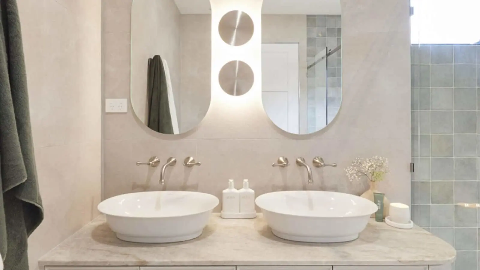 Modern bathroom with dual white vessel sinks, round mirrors, and backlit wall sconce between them.