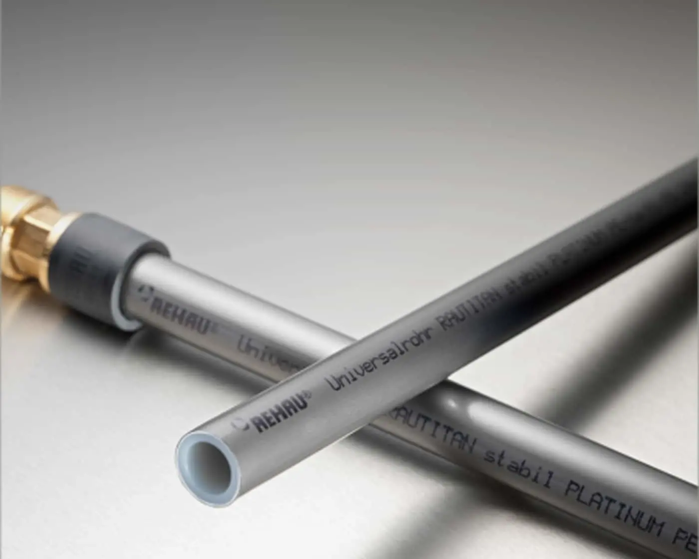 REHAU plumbing pipes with brass fitting, showing gray PEX tubing with blue interior and product text printed on surface.