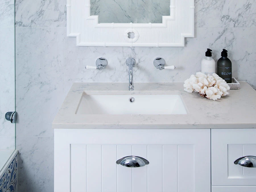 Elegant bathroom vanity with white marble countertop, wall-mounted faucet, decorative coral, and toiletry bottles.