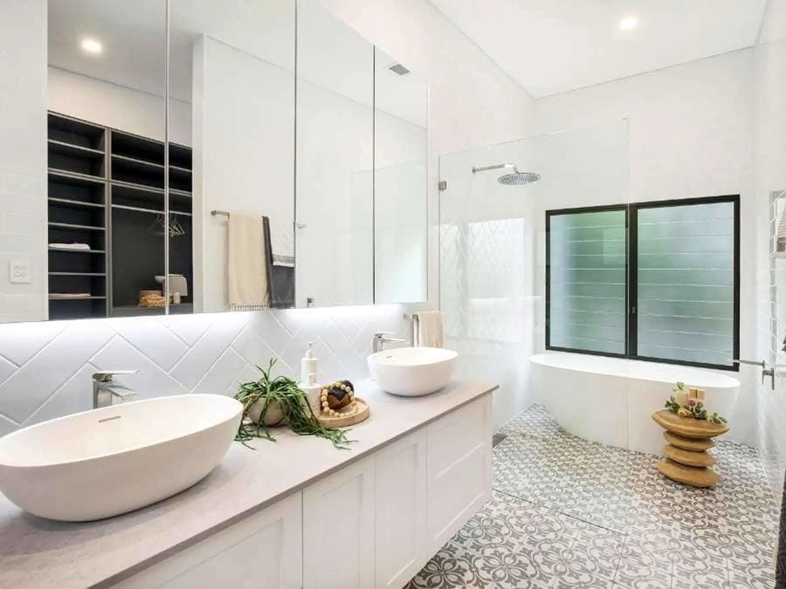 Modern white bathroom with double vessel sinks, patterned floor tiles, glass shower, and black-framed windows.