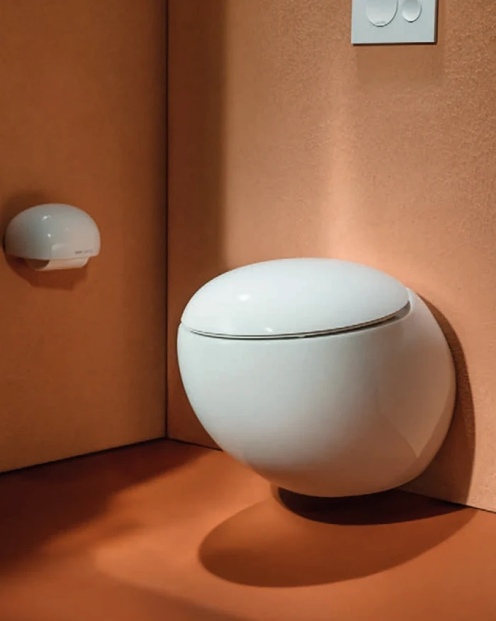 White egg-shaped wall-hung toilet in a terracotta-colored bathroom corner with a matching round toilet paper holder.