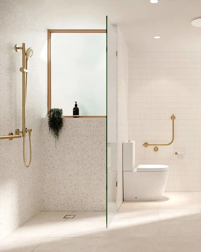 Modern bathroom with glass shower partition, speckled walls, gold fixtures, white toilet, and small plant on shower ledge.