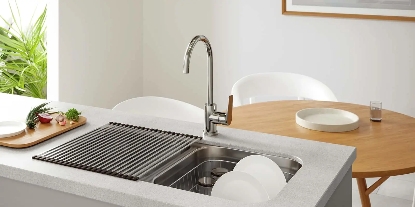 Modern kitchen sink with chrome faucet, white dishes, wooden cutting board, and plant near window.