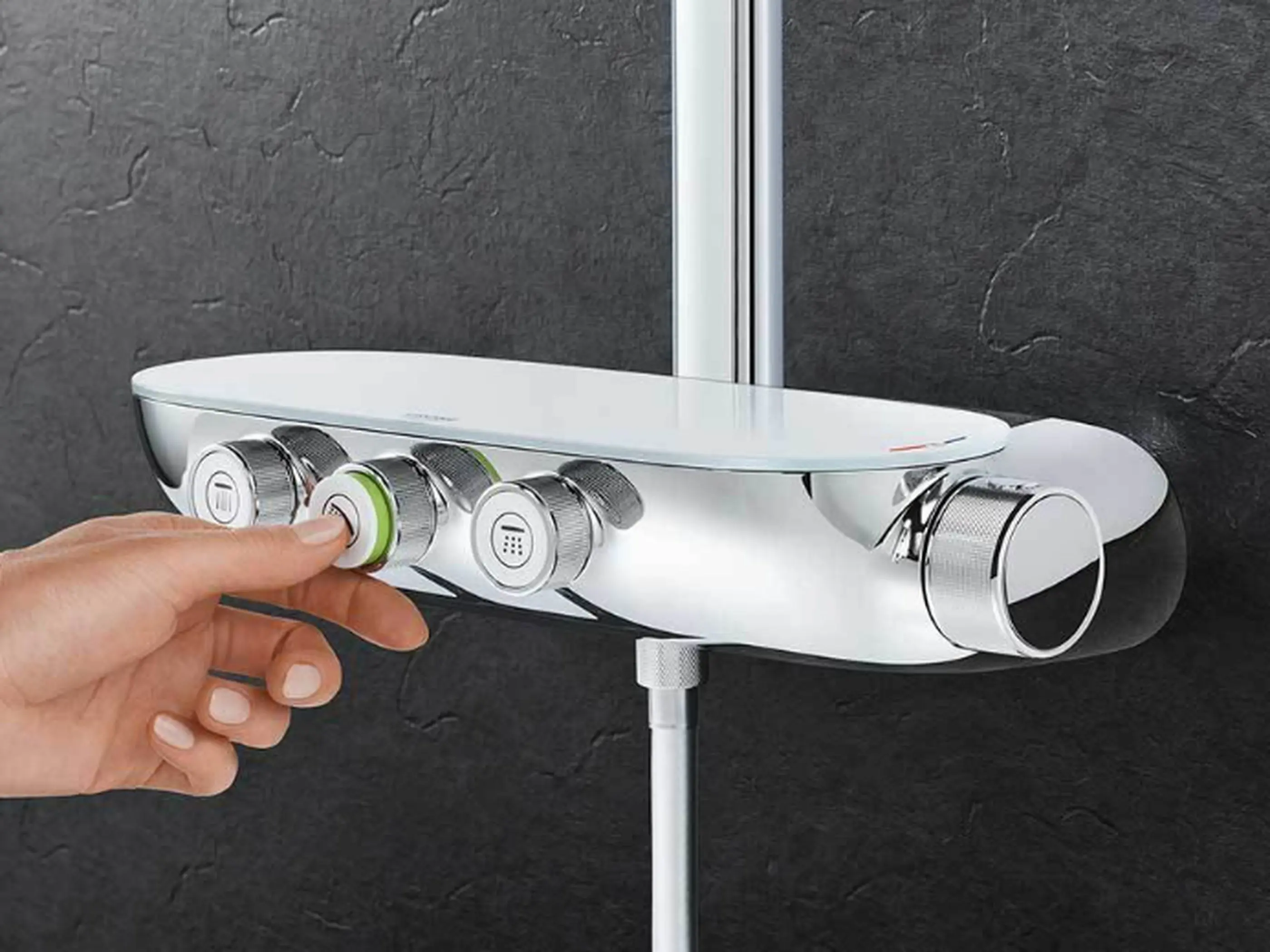 Hand pressing button on modern white shower control panel with multiple dials mounted on dark gray wall.