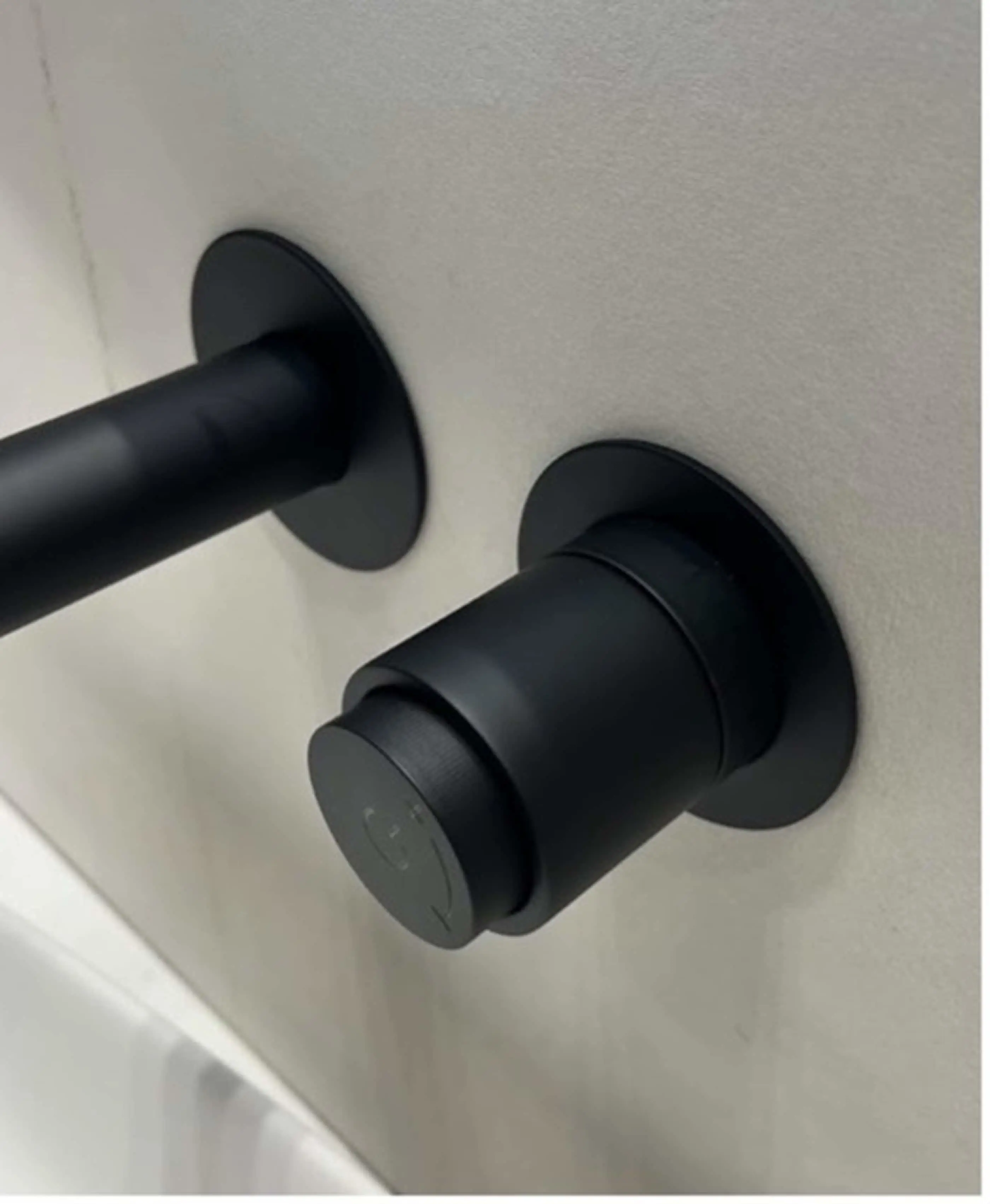 Modern black bathroom faucet with cylindrical handle and spout mounted on white wall.