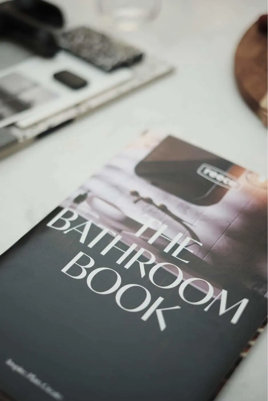 A bathroom design book on a white surface with electronic devices and materials visible in the background.