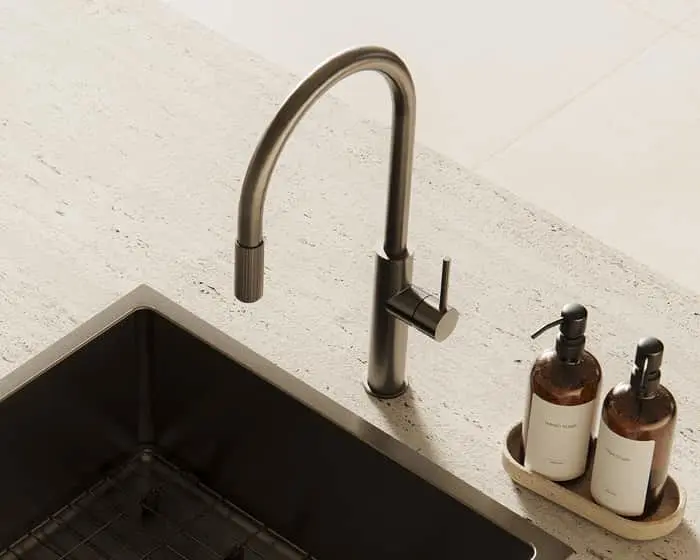 Dark gunmetal kitchen faucet with pull-down sprayer on a stone countertop beside a dark undermount sink and two soap dispensers.
