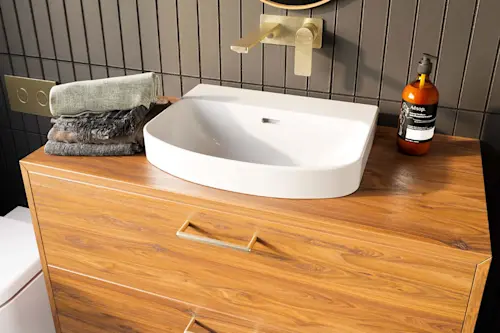Modern bathroom vanity with white basin sink, brass wall-mounted faucet, folded towels, and Aesop soap on wooden cabinet.