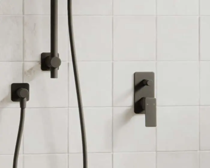 Modern shower with matte black fixtures and controls mounted on white tiled wall.
