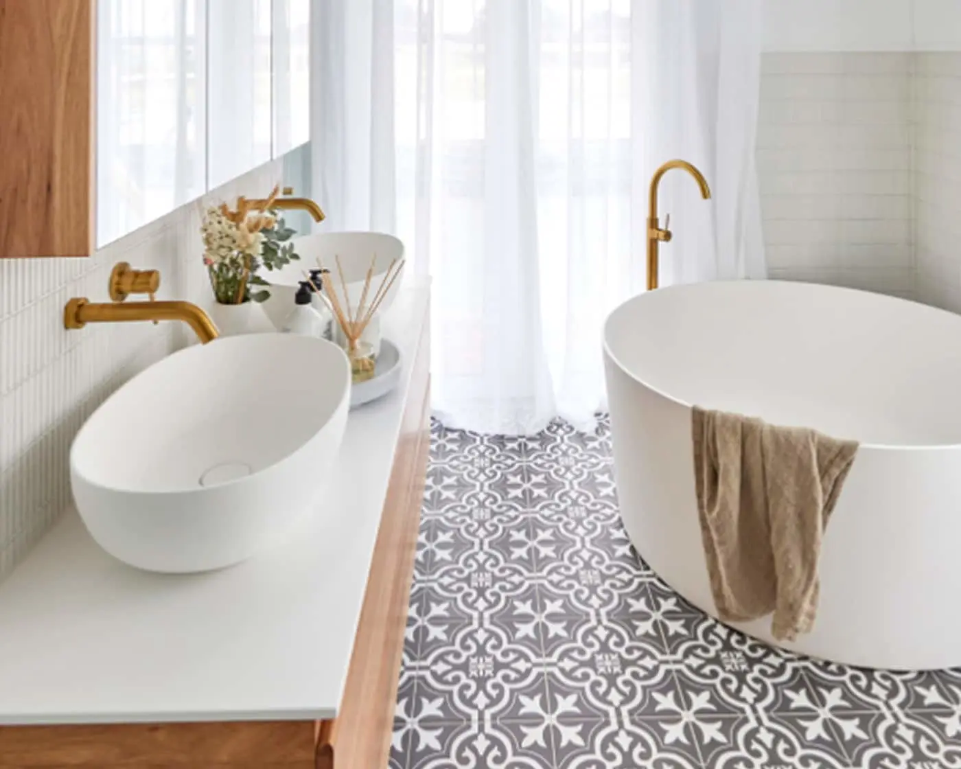 Modern bathroom with white oval tub, vessel sink, brass fixtures, patterned floor tiles, and sheer white curtains.