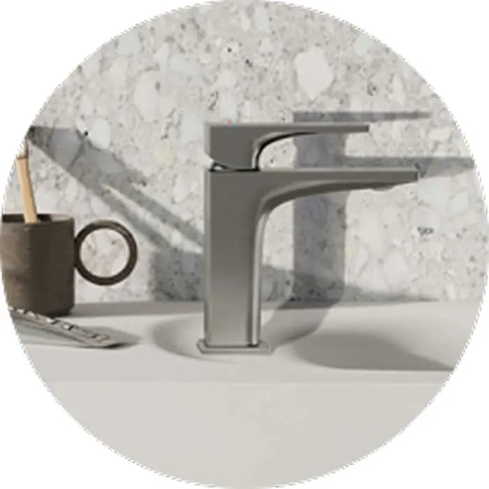 Modern gray bathroom faucet mounted on white sink with marble backsplash and small container in background.