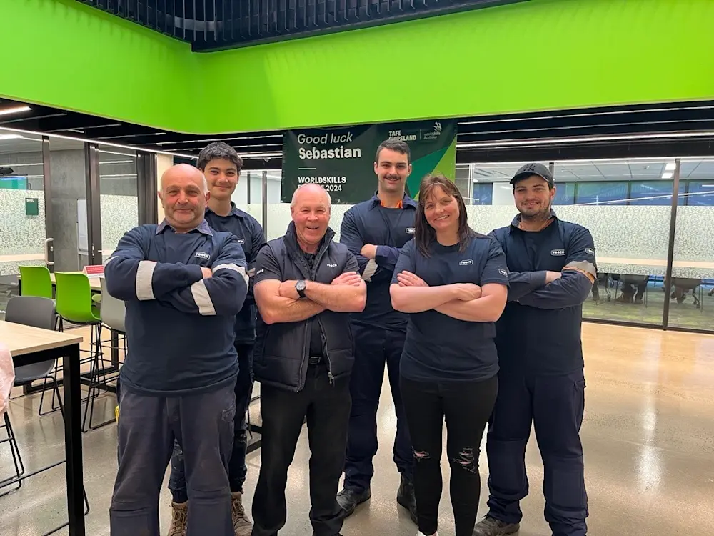 Group of people in navy uniforms standing with arms crossed in front of a WorldSkills 2024 banner with bright green walls.
