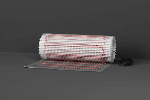 Electric floor heating mat with red wiring partially rolled out on gray background with power connector visible.