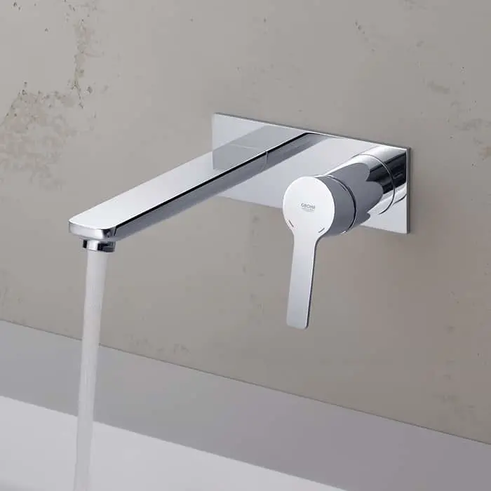 Modern chrome wall-mounted bathroom faucet with long spout and single lever handle, water flowing from tap.