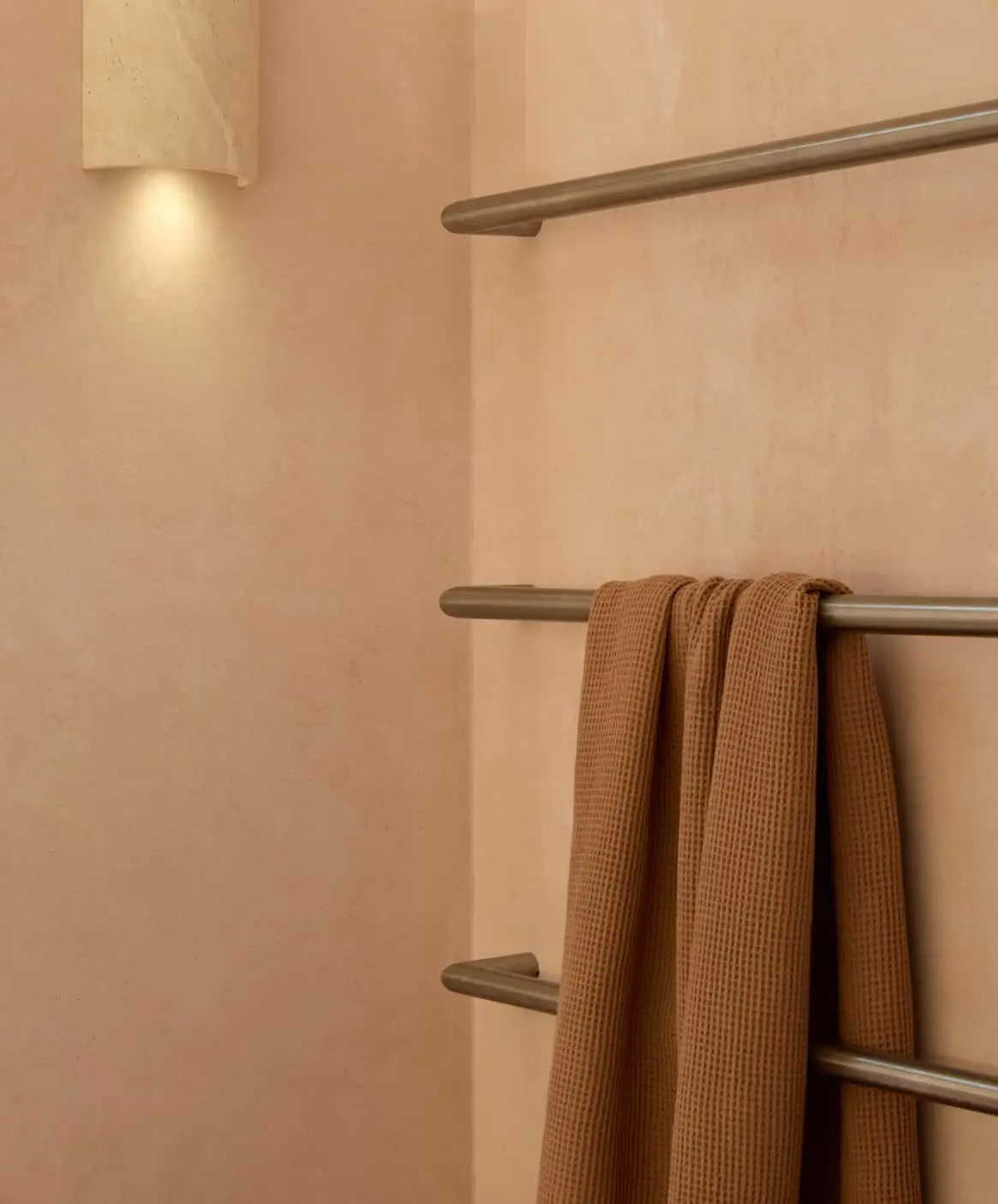 Brown waffle-textured towel hanging on a metal towel rack against a peach-colored wall with soft lighting.