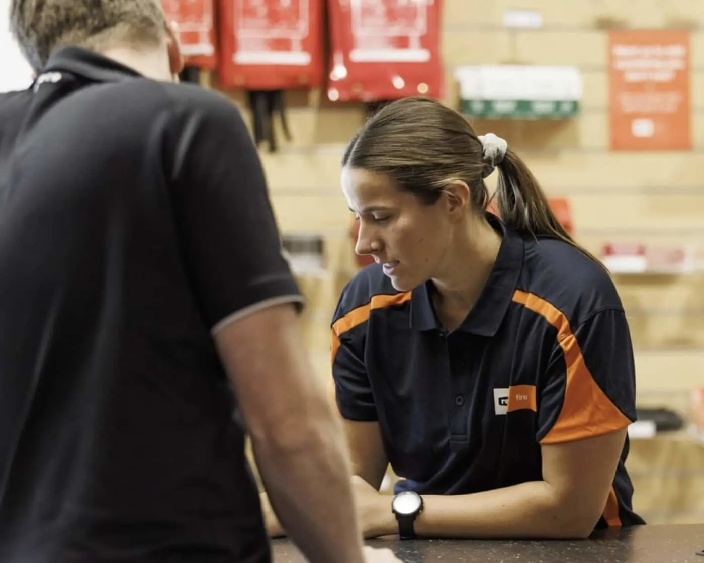 Reece employee in navy uniform assisting a customer at counter with red signage in background.