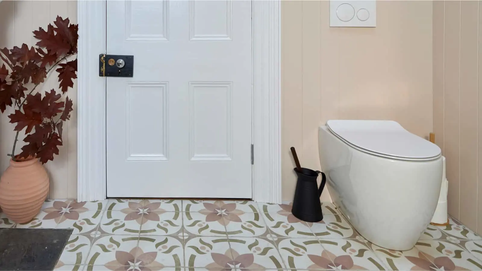 Modern bathroom with white toilet, floral patterned floor tiles, white door, and terracotta pot with red maple leaves.
