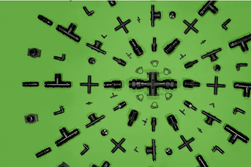 Black plumbing or irrigation fittings arranged on bright green background, featuring T-joints, connectors, and cross pieces.