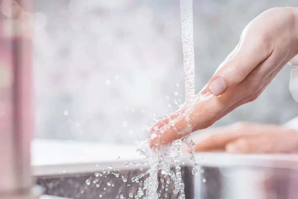 Hand washing under running water with splashing droplets in a bathroom sink.