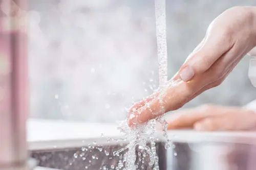 Hand washing under running water with splashing droplets in a bathroom sink.