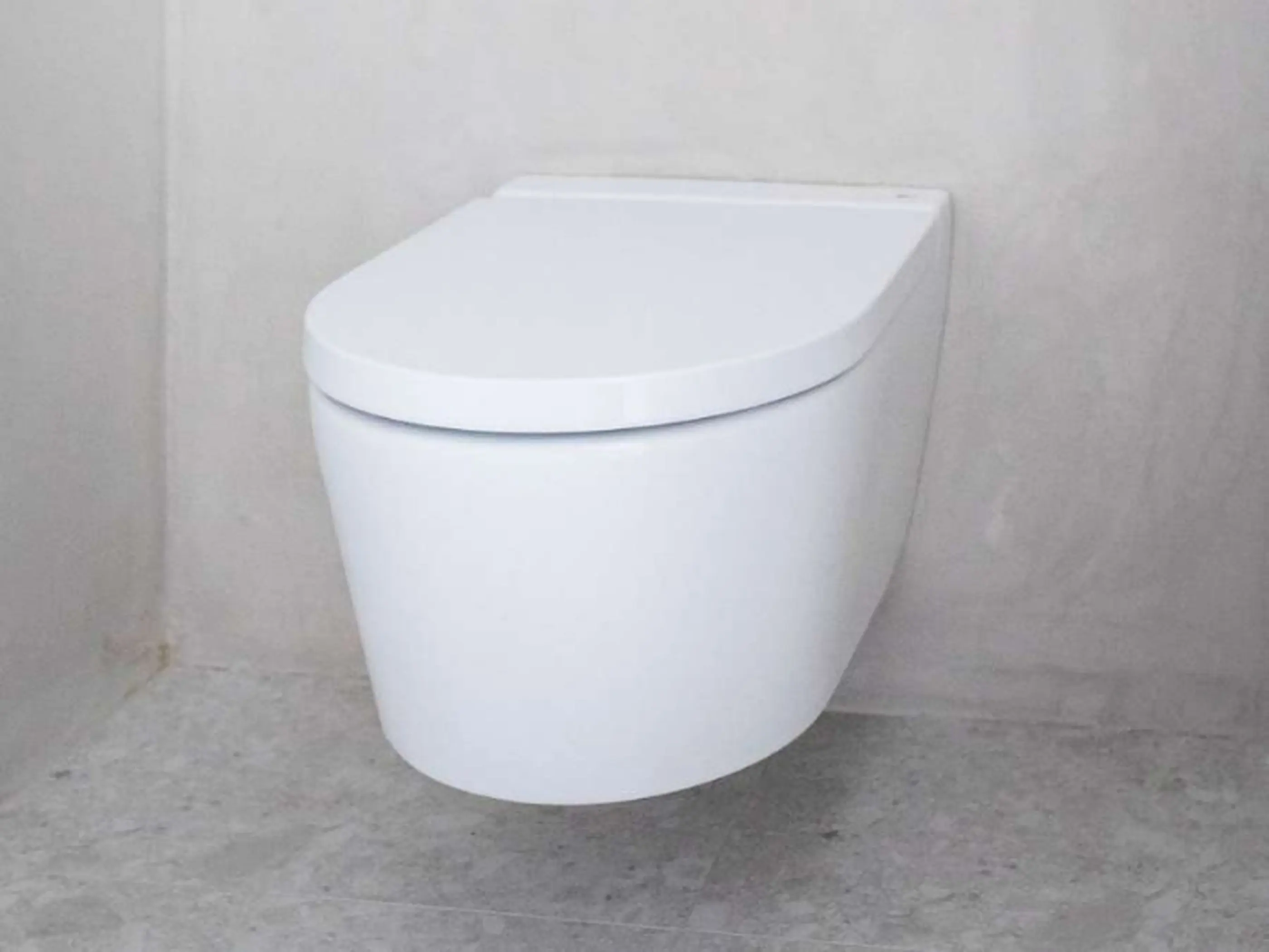Modern white wall-mounted toilet with closed lid against light gray walls and concrete floor.