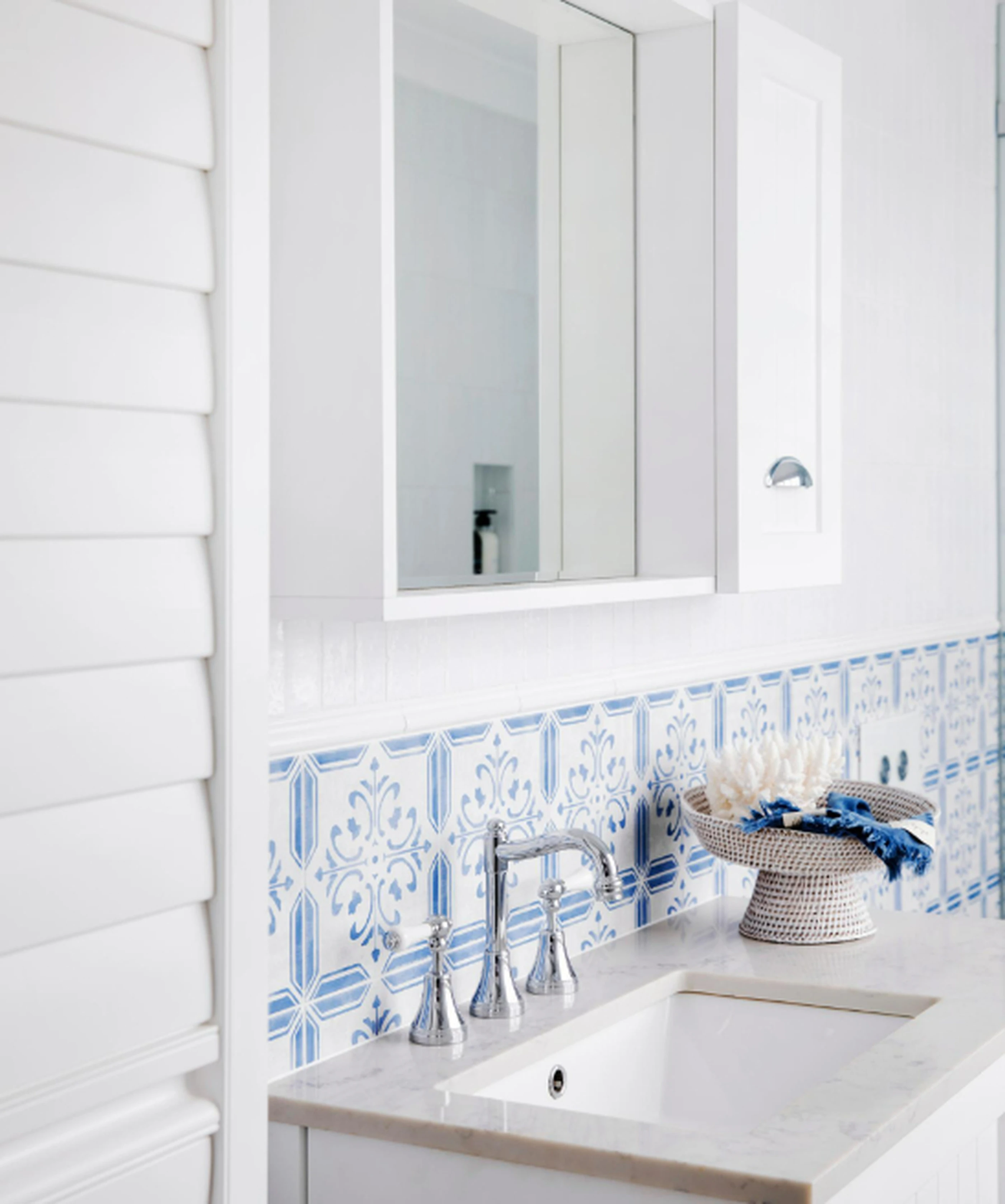 White bathroom with blue and white patterned tile backsplash, chrome faucet, white sink, and medicine cabinet mirror.
