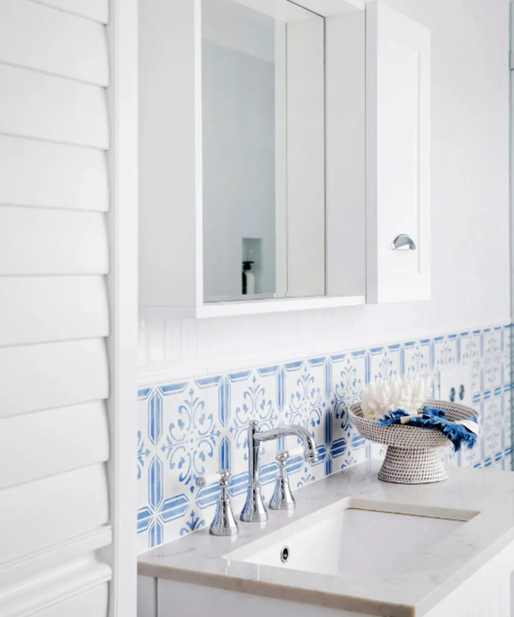 White bathroom with blue and white patterned tile backsplash, chrome faucet, white sink, and medicine cabinet mirror.