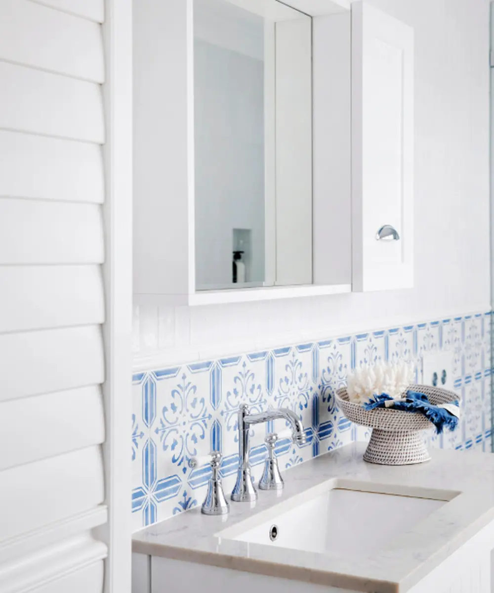 White bathroom with blue and white patterned tile backsplash, chrome faucet, white sink, and medicine cabinet mirror.