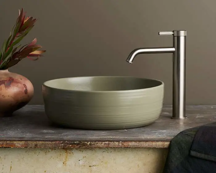 Modern bathroom sink with sage green ceramic bowl basin, stainless steel faucet, and decorative vase with red flowers.