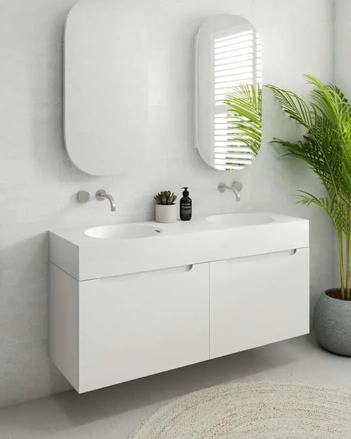 Modern white bathroom vanity with double sink, oval mirrors, wall-mounted faucets, and a potted palm plant.