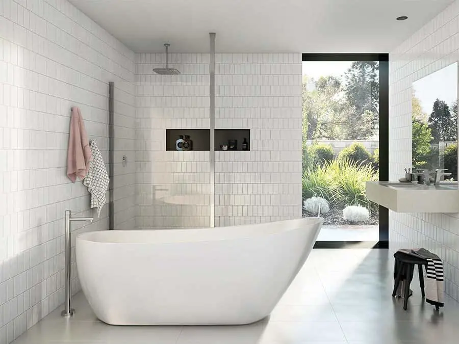 Modern white bathroom with freestanding tub, walk-in shower, and large window overlooking garden landscape.