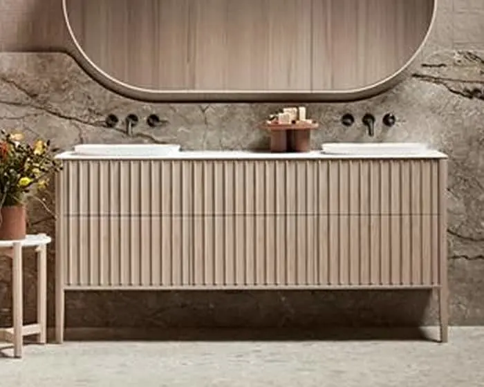 Modern bathroom vanity with fluted wooden cabinet, oval mirror, stone wall backdrop, and small potted plant.