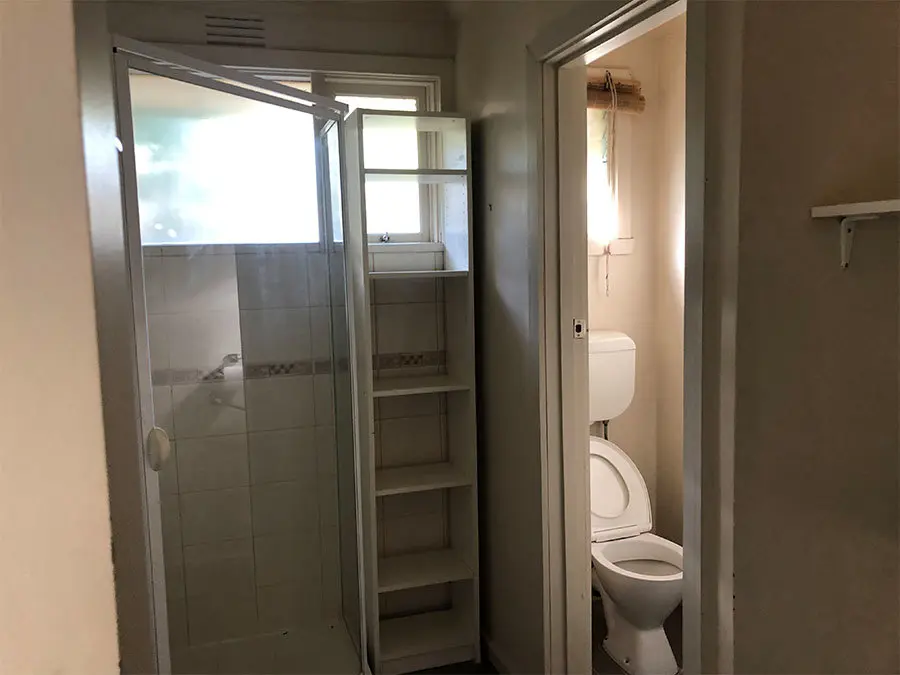 Small bathroom with glass shower stall on left, toilet in separate compartment on right, and built-in shelving.
