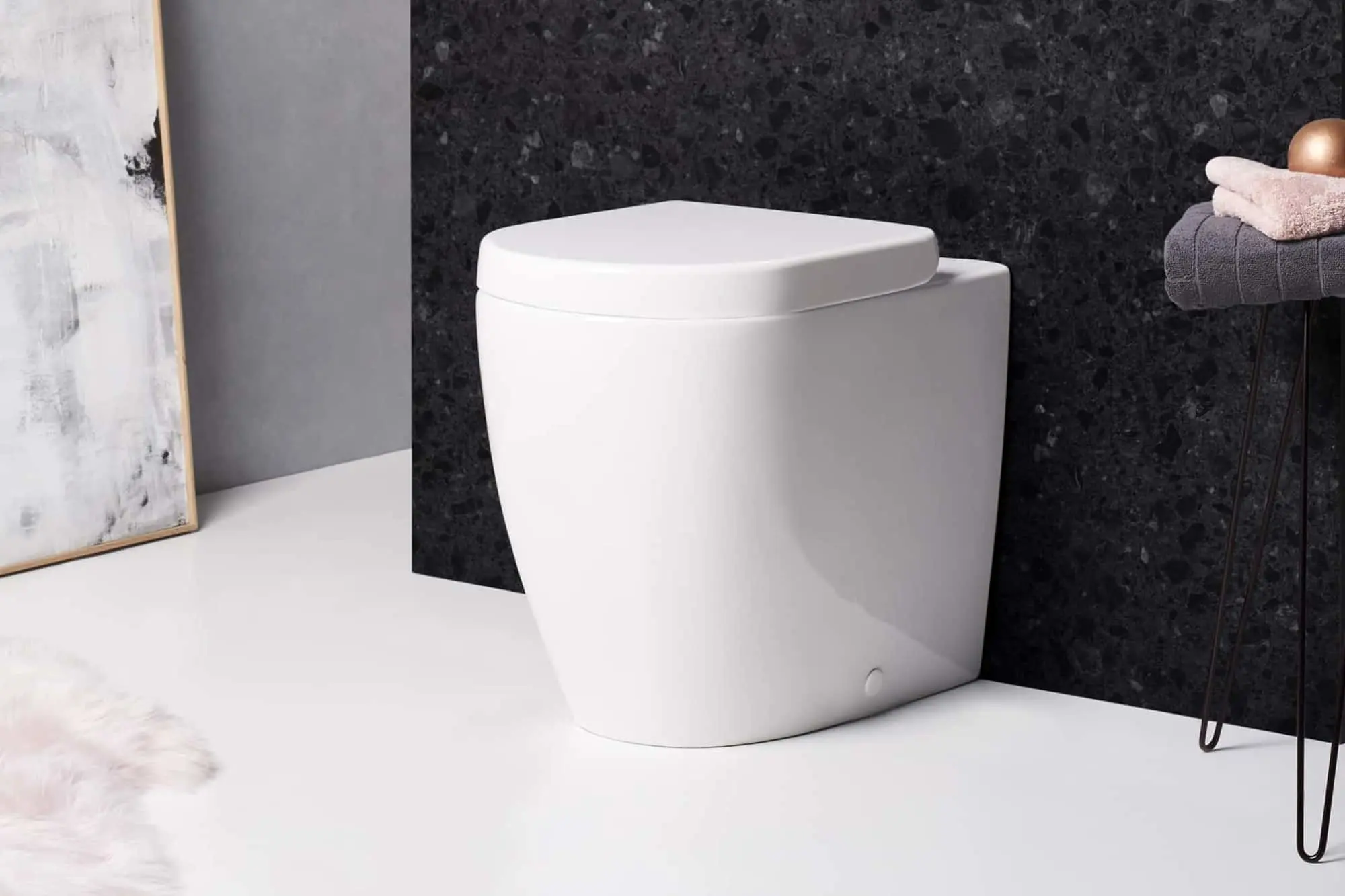 White back-to-wall toilet against a dark granite wall, with folded towels on a stool nearby.