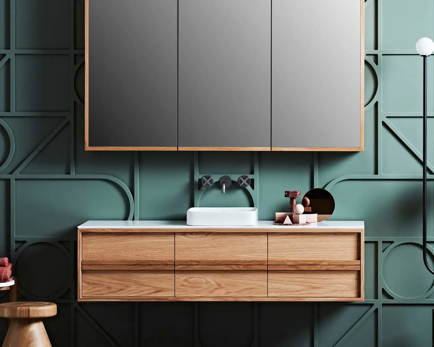 Modern bathroom with wooden vanity, white sink, and mirrored cabinet against teal geometric wall panels.