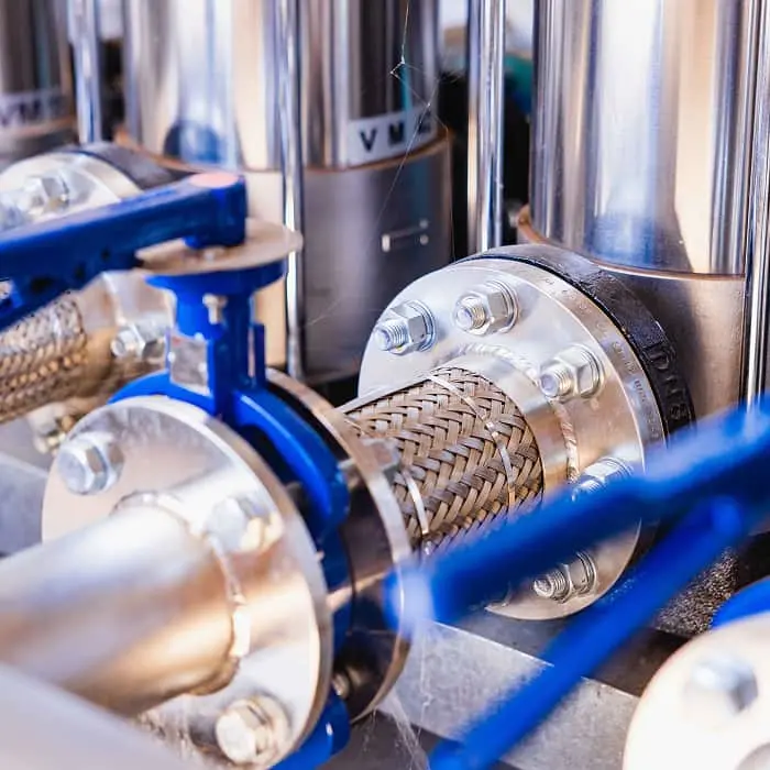 Close-up of industrial metal pipes with blue valves and braided metal hoses connected with flanges and bolts.