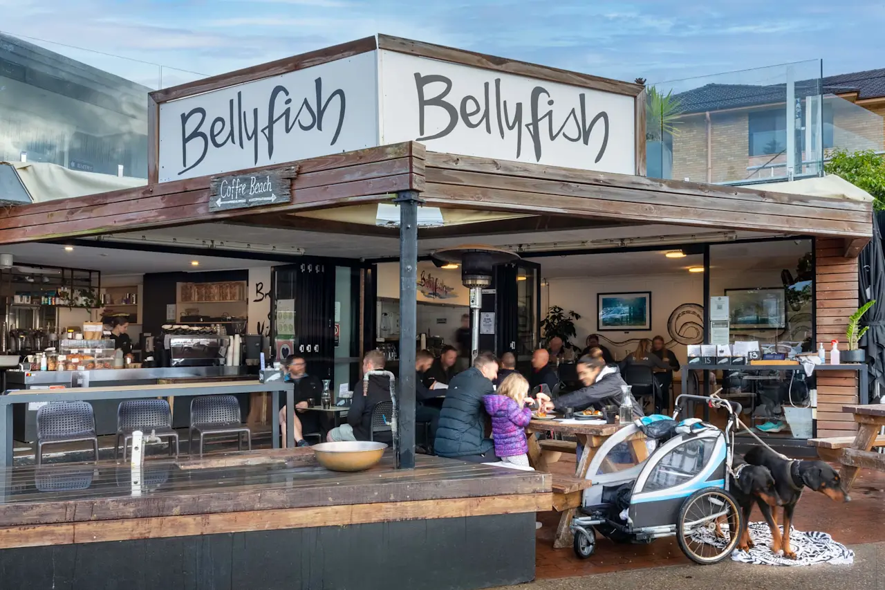 Bellyfish café with wooden exterior, outdoor seating area filled with customers, and a dog standing next to a child's bike trailer.