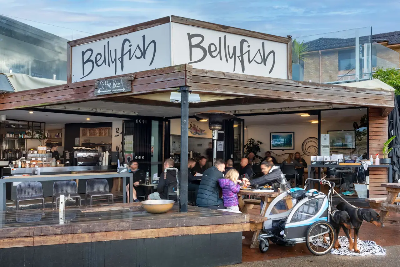 Bellyfish café with wooden exterior, outdoor seating area filled with customers, and a dog standing next to a child's bike trailer.