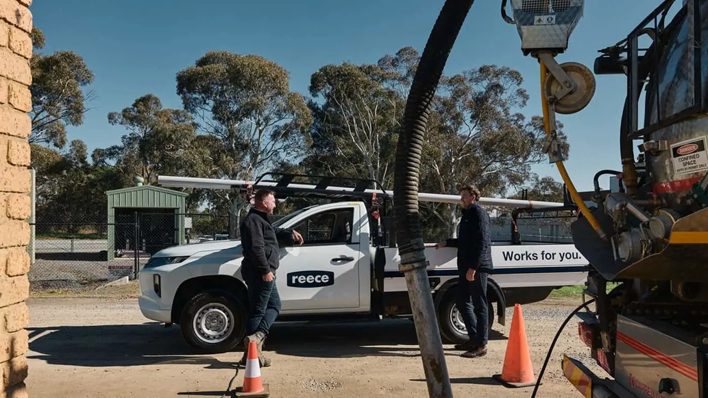 Two workers standing beside a white Reece utility truck with drilling equipment at a rural worksite under blue sky.