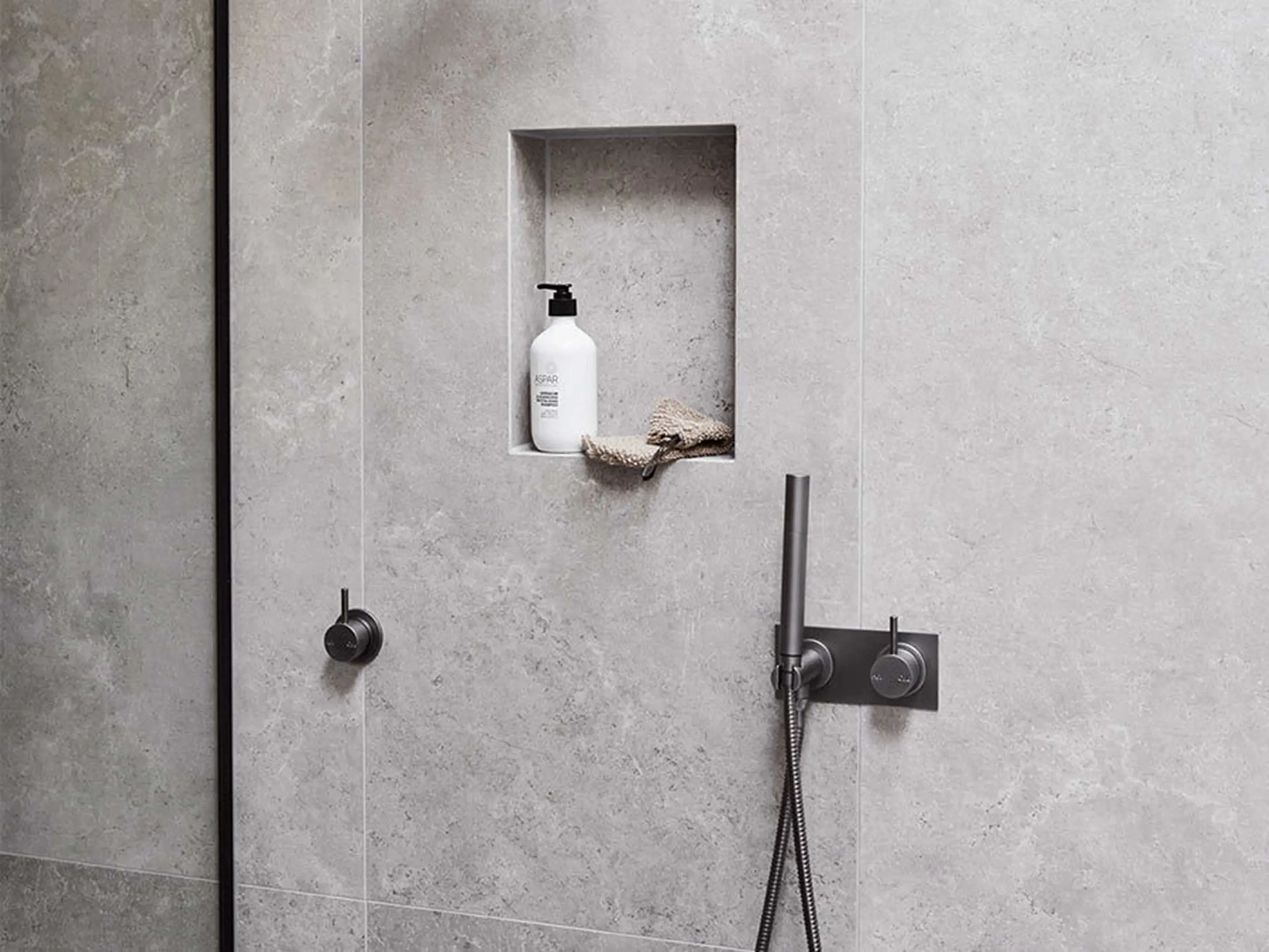 Modern shower with gray concrete walls, built-in niche holding white soap dispenser, and black metal fixtures.
