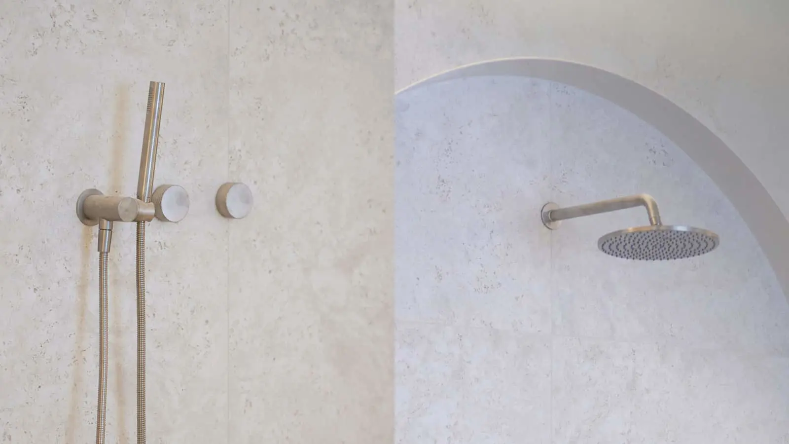 Modern bathroom with brushed metal fixtures including handheld shower attachment and rainfall showerhead in arched alcove.