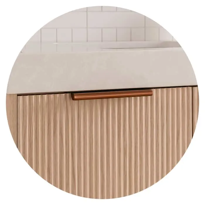Close-up of wooden cabinet with vertical ribbed pattern and copper handle beneath white countertop in bathroom setting.