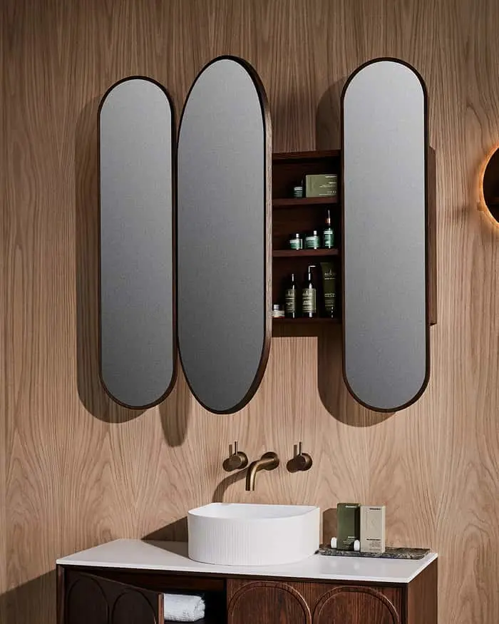Modern bathroom with three oval mirrors, one open to reveal shelved storage, above a white vessel sink and wooden vanity.
