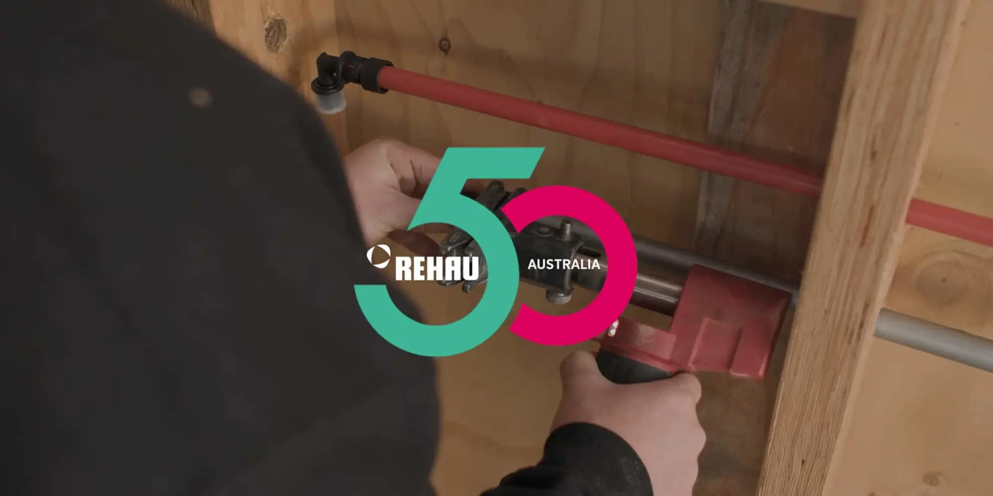 Person installing red plumbing pipe with REHAU 50 Australia logo overlay in turquoise and pink.