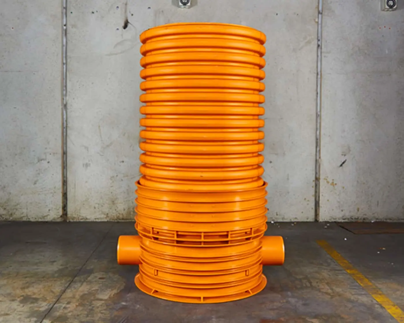 Bright orange cylindrical inspection chamber with ribbed exterior standing against a concrete wall.