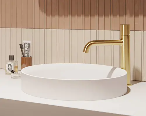Modern bathroom sink with gold faucet, toothbrush holder, and perfume bottles against pink and cream tiled wall.