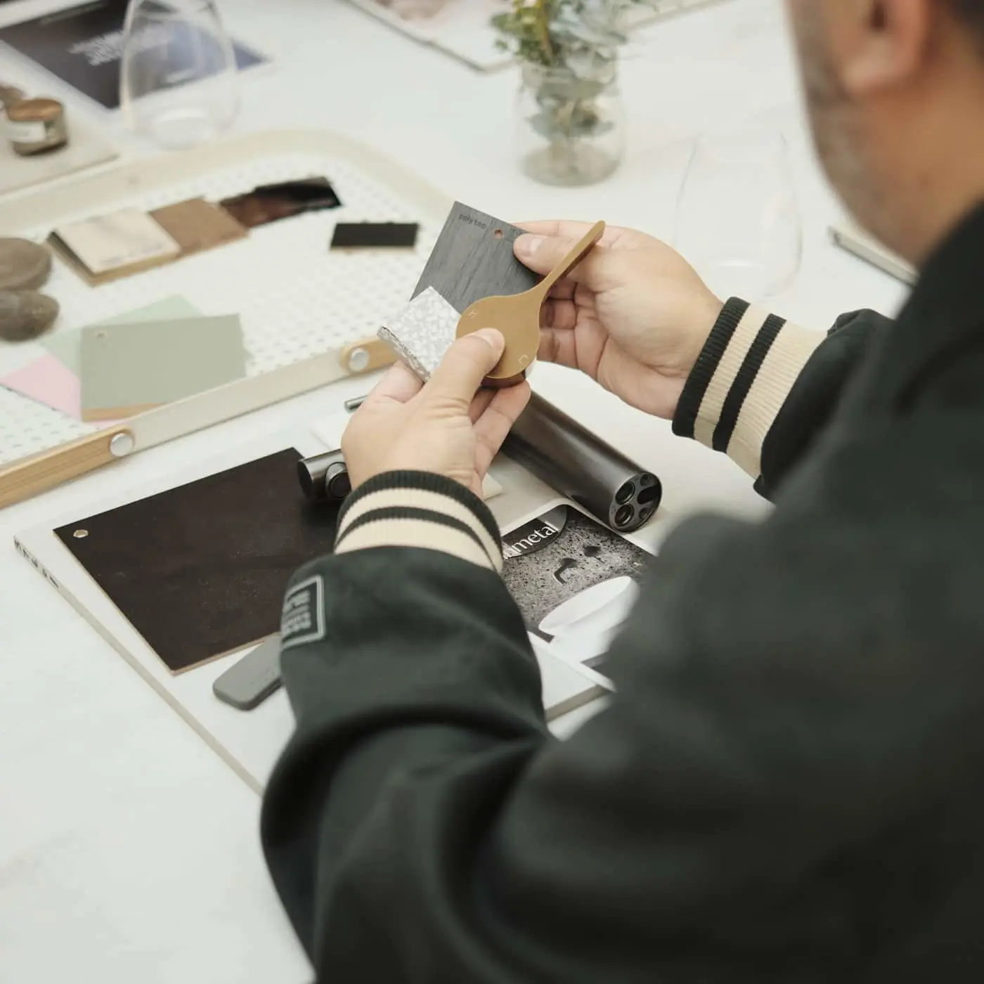 Person holding material swatches over a table covered with various design samples, color swatches, and material boards.