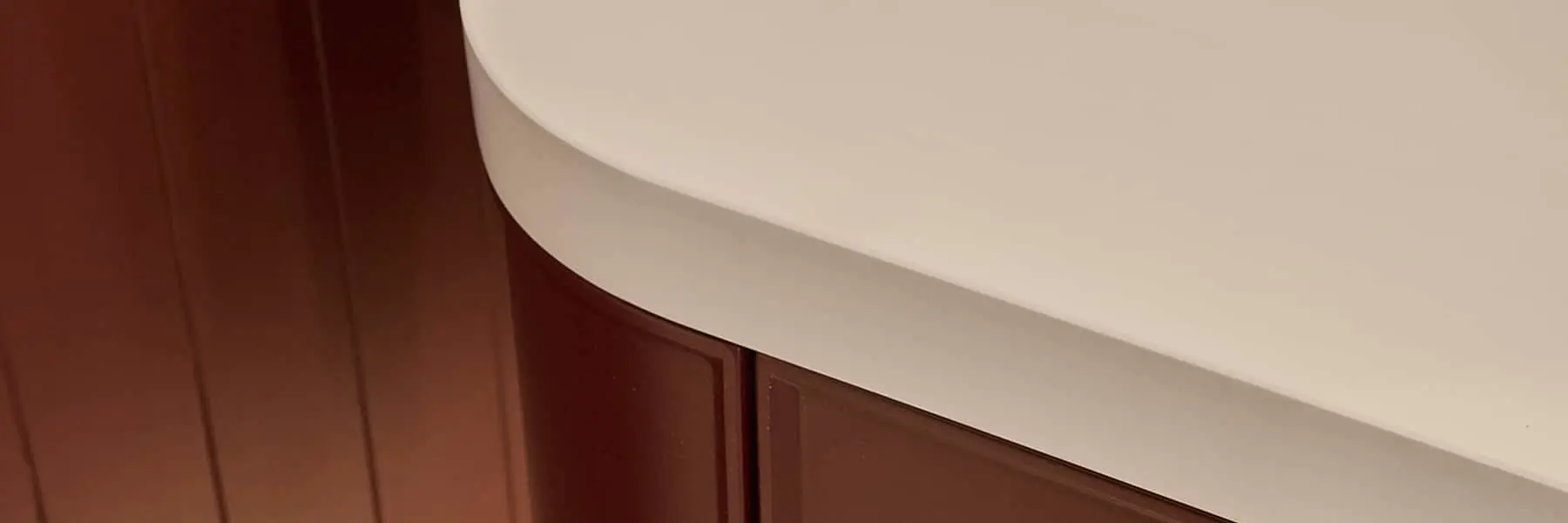 Close-up of a curved white countertop or surface meeting dark wood cabinetry, showing contrast between materials.